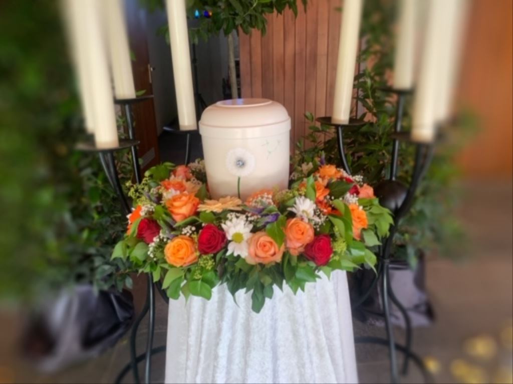 Urne mit Blumenkranz zwischen Kerzen